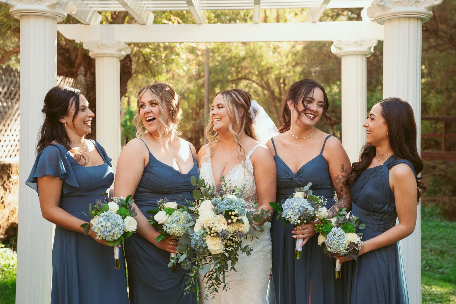 Bridesmaids in navy blue dresses hold matching bouquets while posing together outdoors.