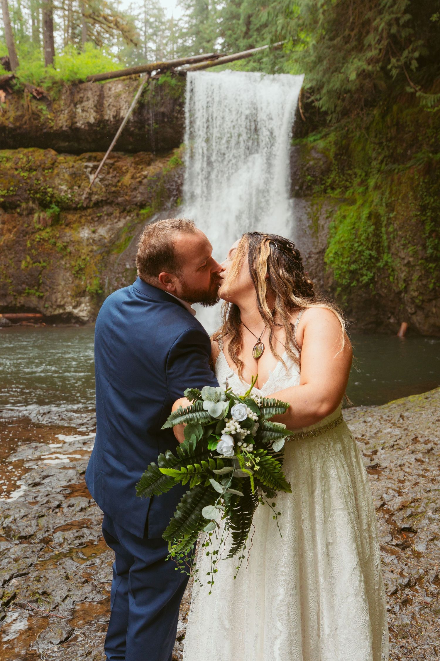Intimate wedding moments photographed by a serene waterfall in a Pacific Northwest forest.