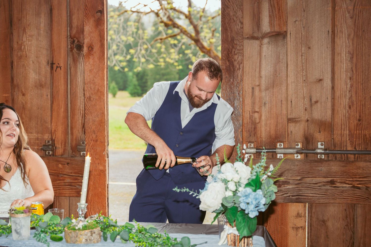 Candid moments during a barn wedding reception with elegant table settings and greenery.