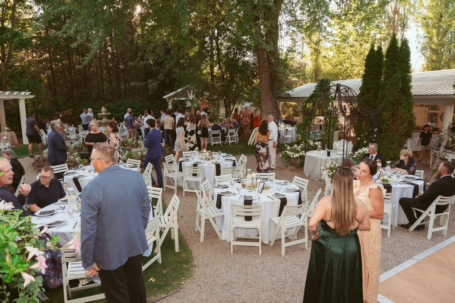 Outdoor wedding reception setup with white chairs and decorations in a garden setting.