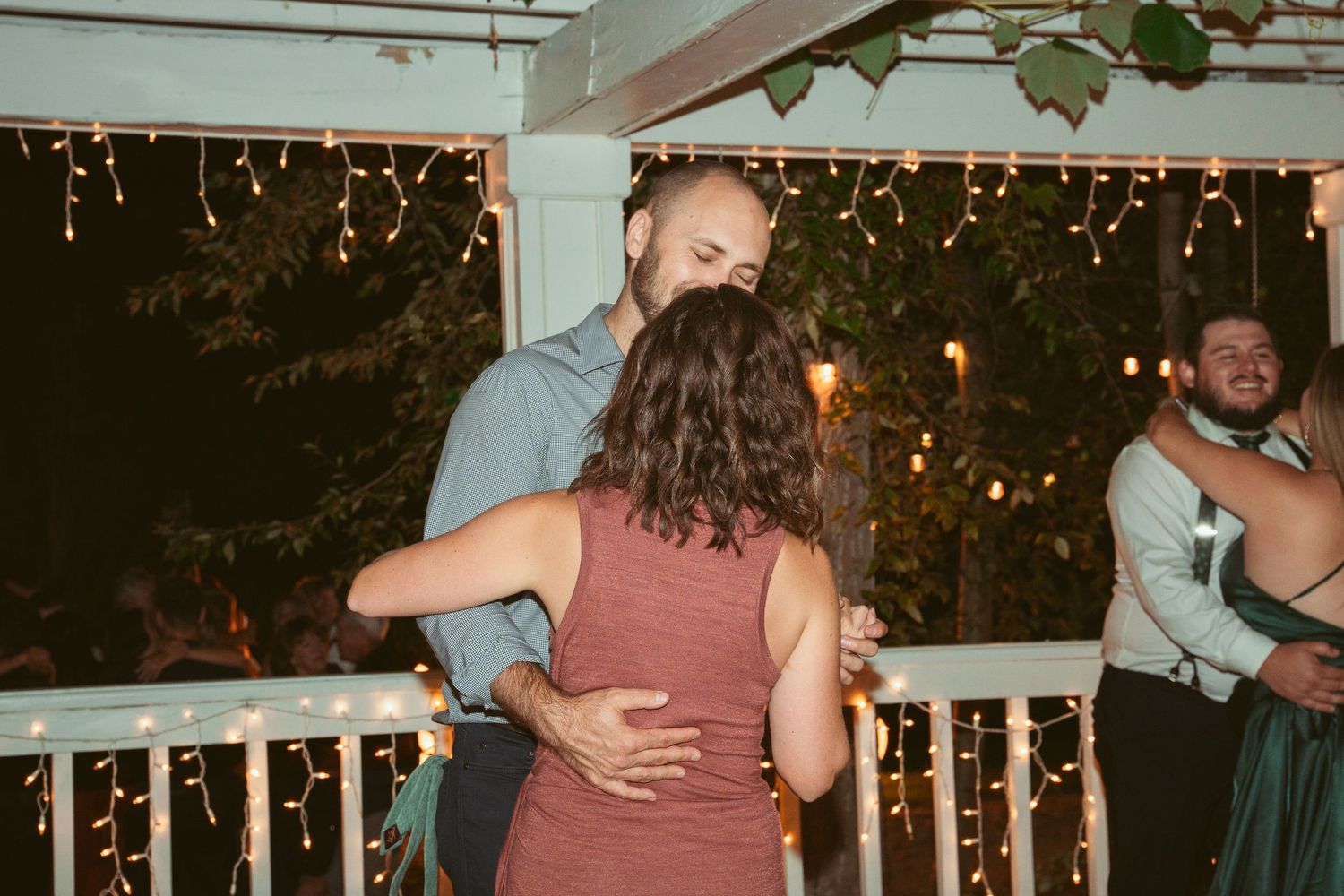 People embracing and dancing under string lights at an outdoor evening celebration.