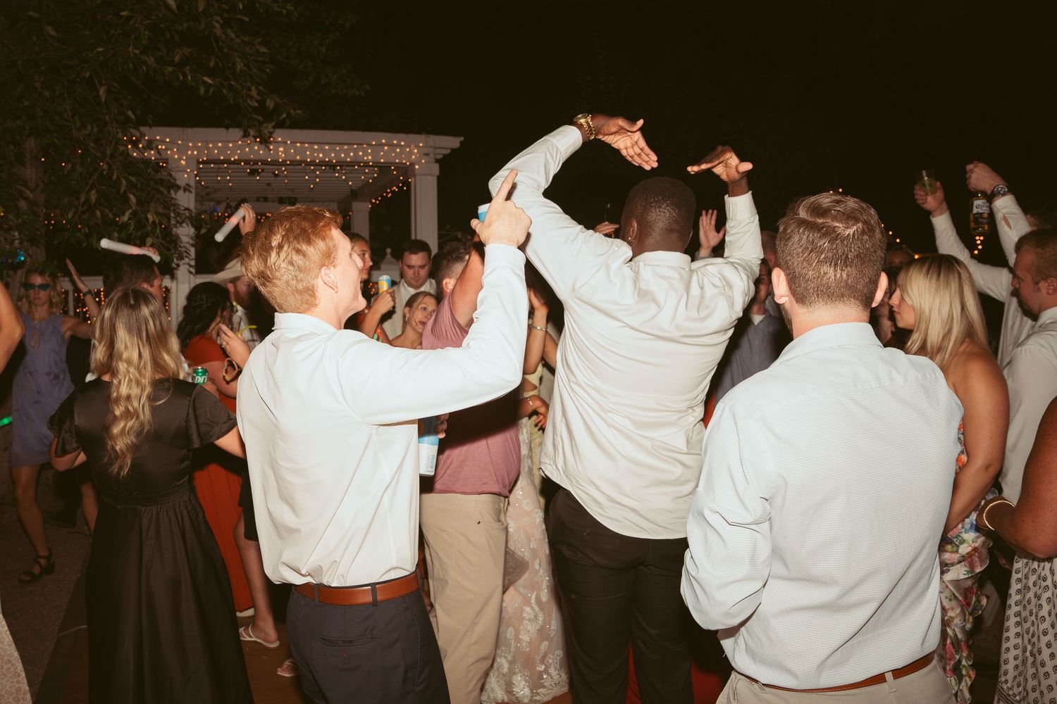 Guests dancing with raised arms at an outdoor evening celebration.