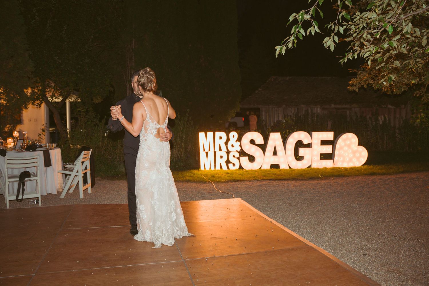 Evening wedding celebration with lit signage and guests dancing on outdoor patio.