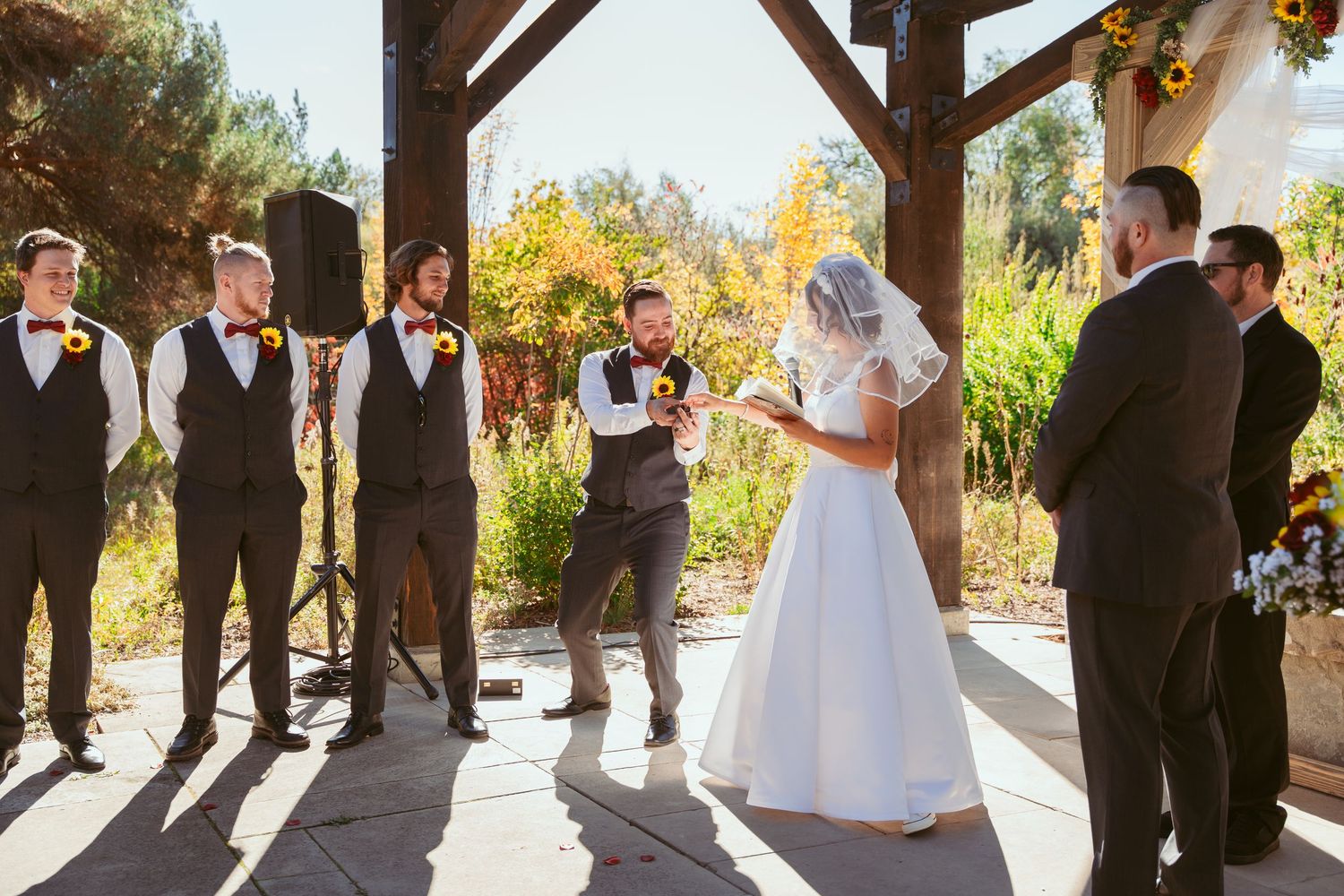 Wide angle shot of wedding party gathered under covered outdoor ceremony space.