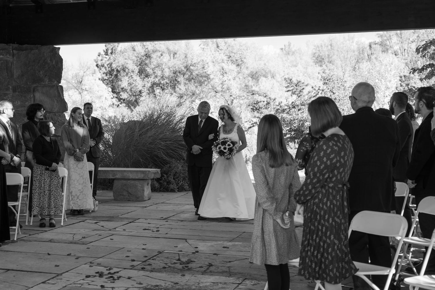 Black and white photo of wedding ceremony with guests gathered on stone patio under covered area.
