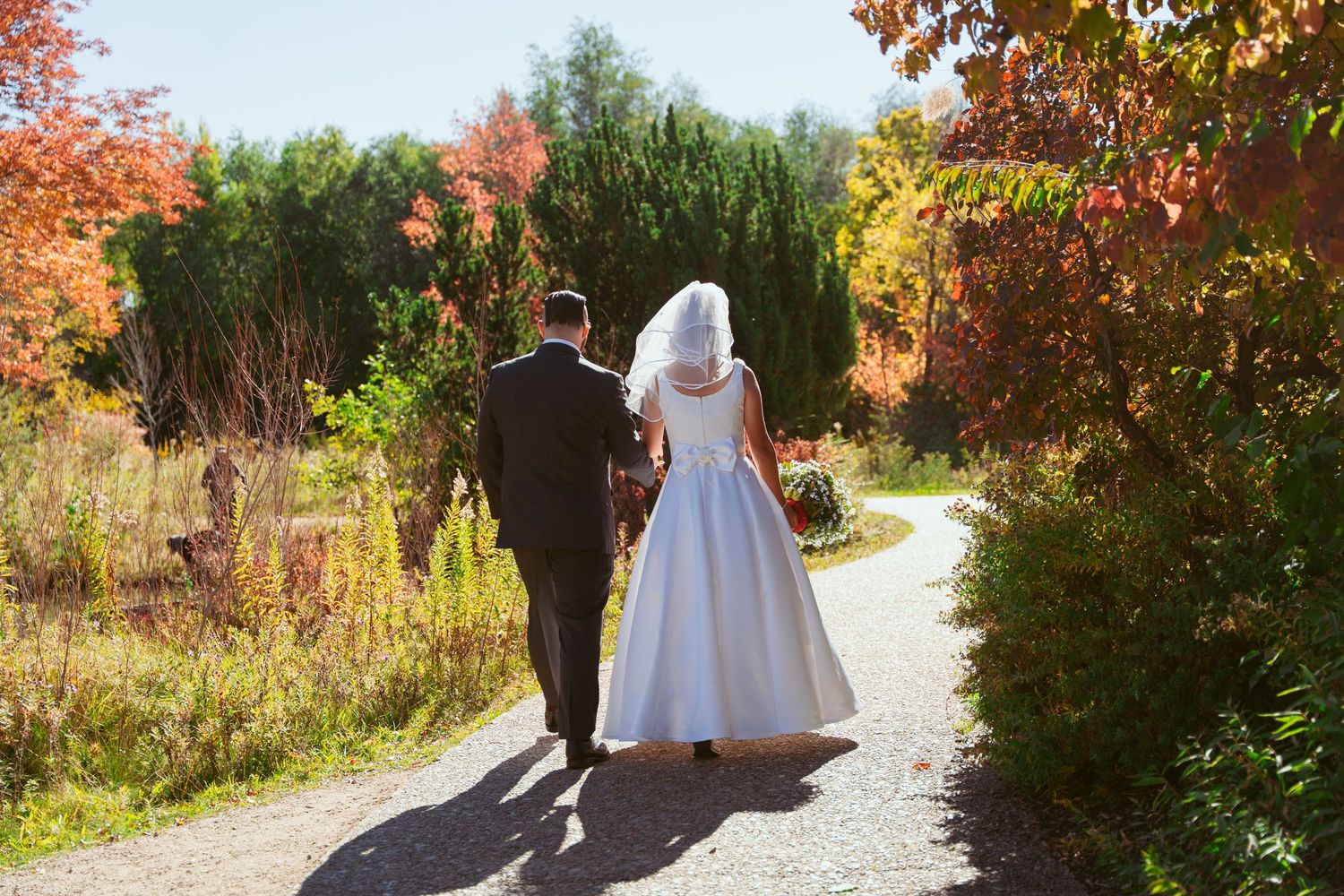 Wedding party walking along an autumn path with vibrant fall foliage in the background.