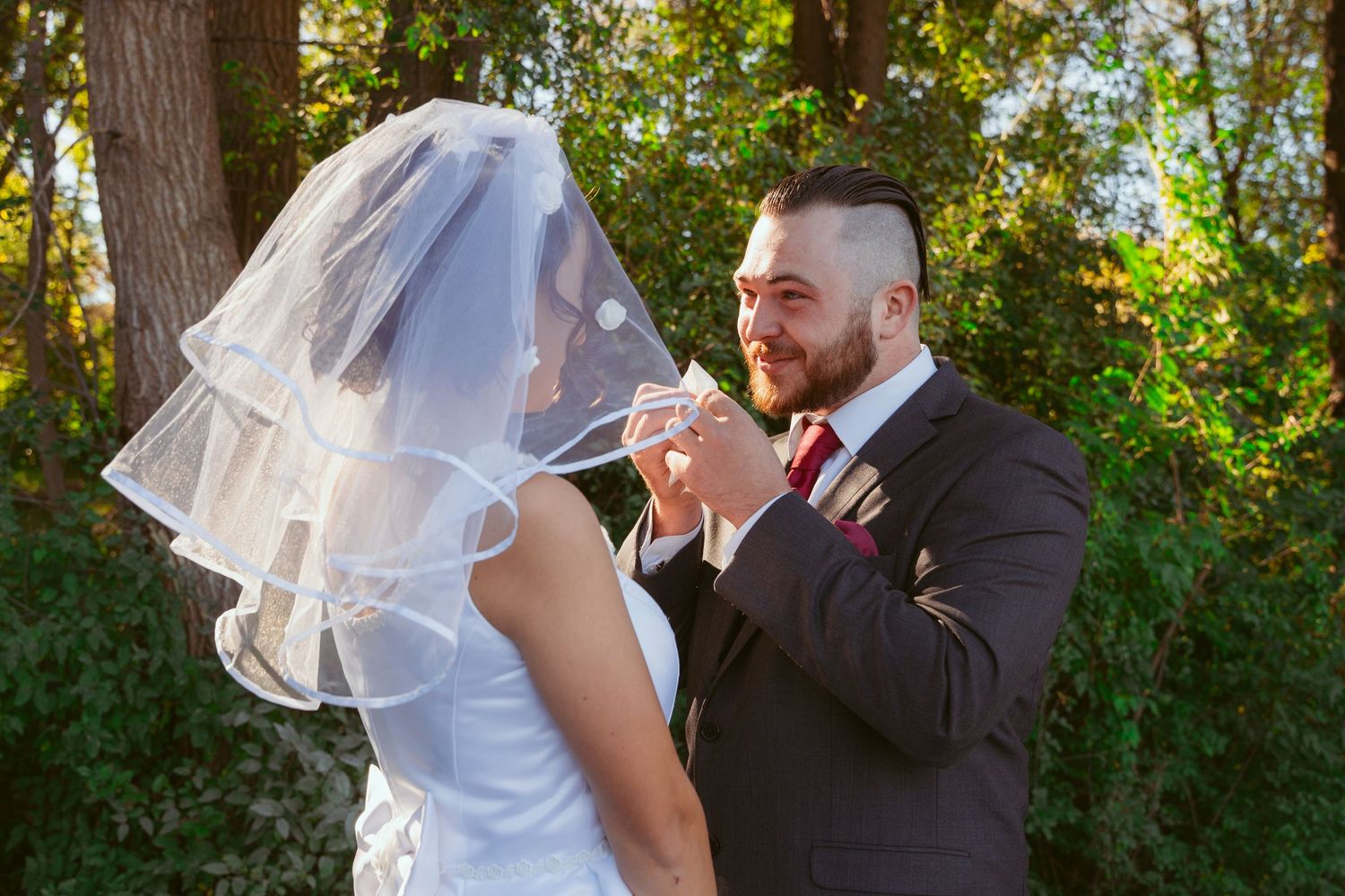 Sunlit outdoor wedding scene showing a couple's intimate moment among trees.