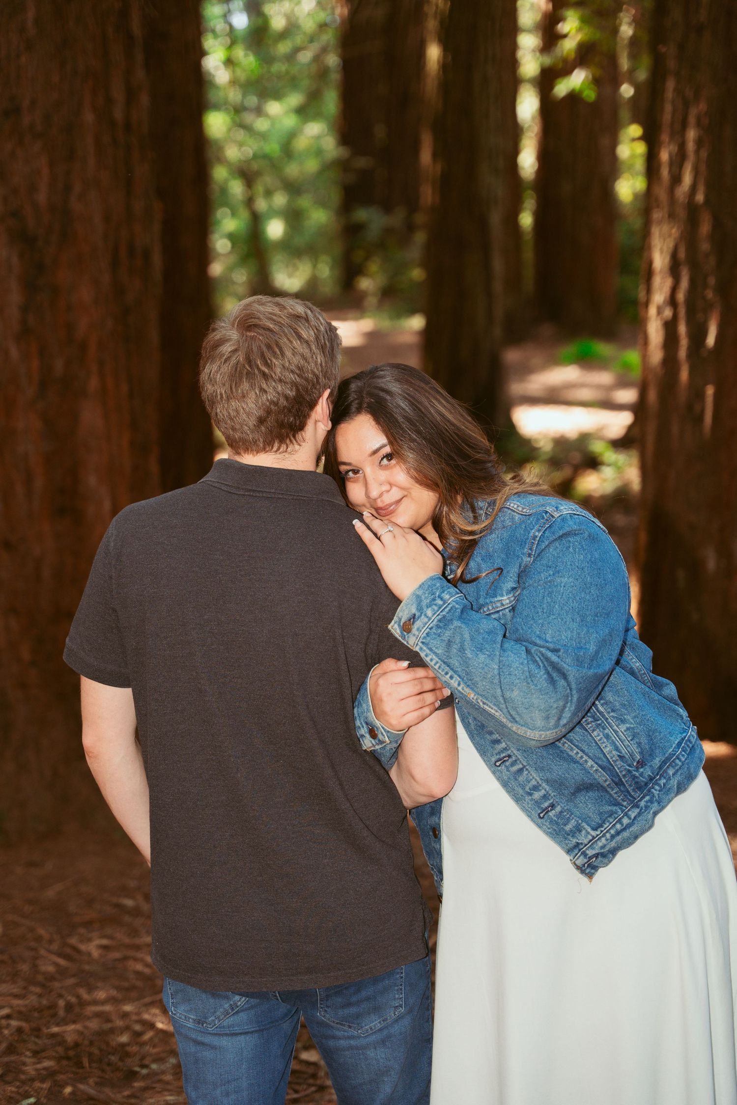A couple embraces while walking through a serene redwood forest on a sunny afternoon.