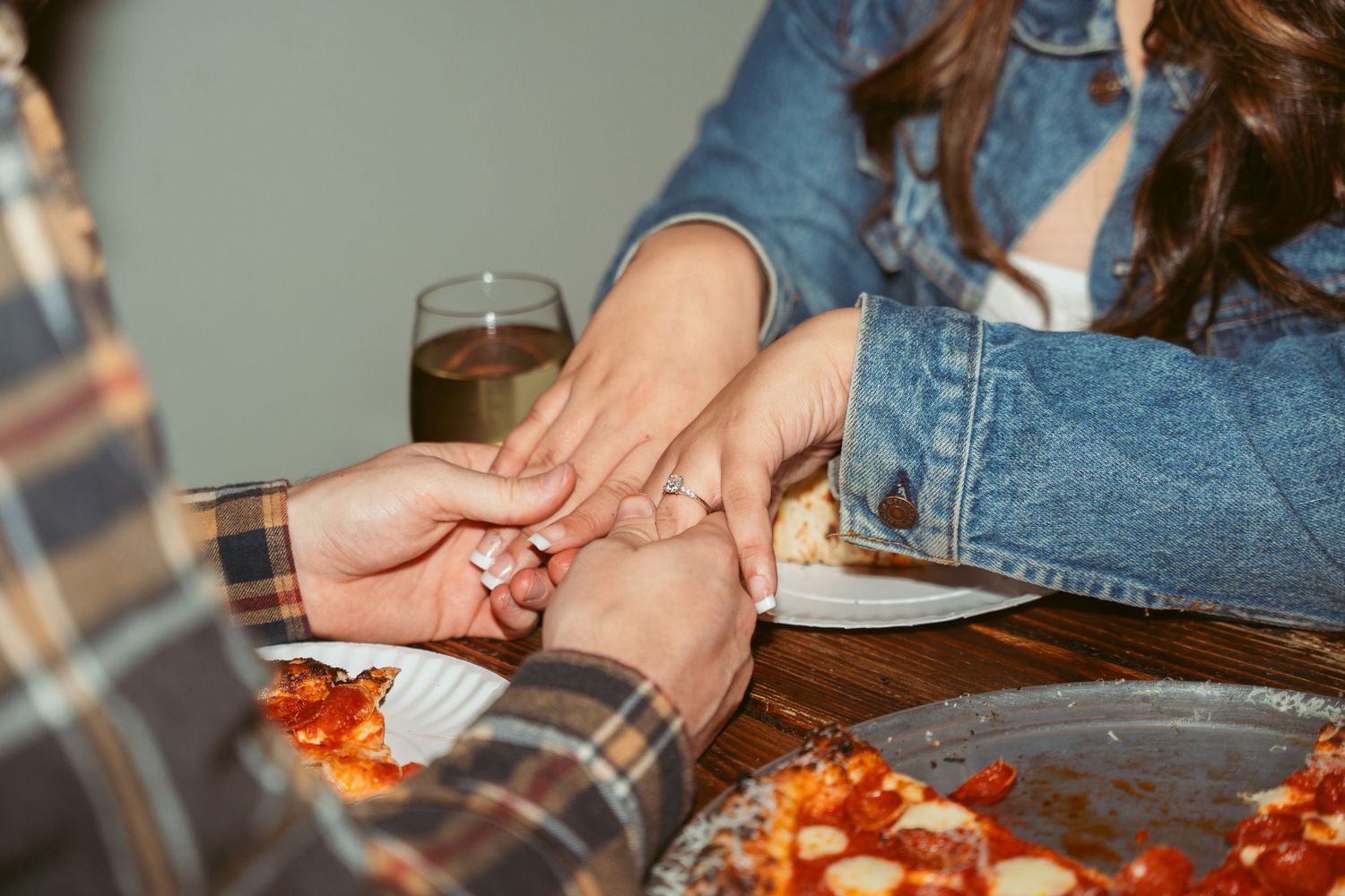 Close-up of hands reaching for slices of fresh pizza on a wooden table.