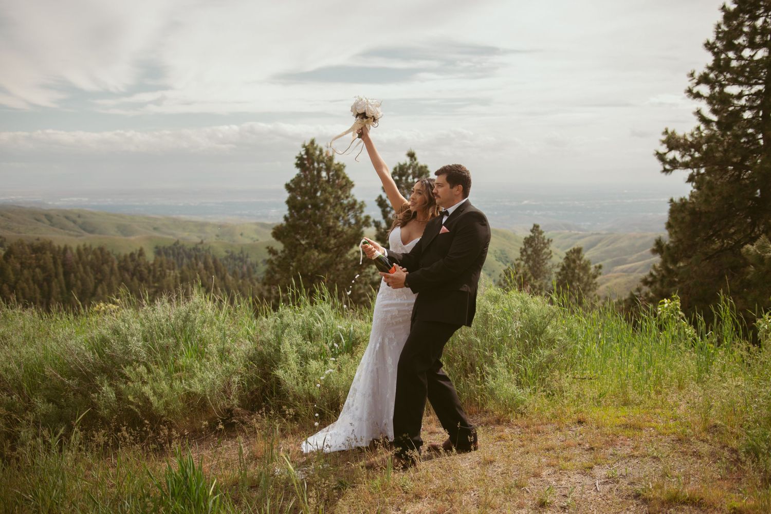 Newlyweds dancing and celebrating on a mountain ridge with dramatic landscape views.