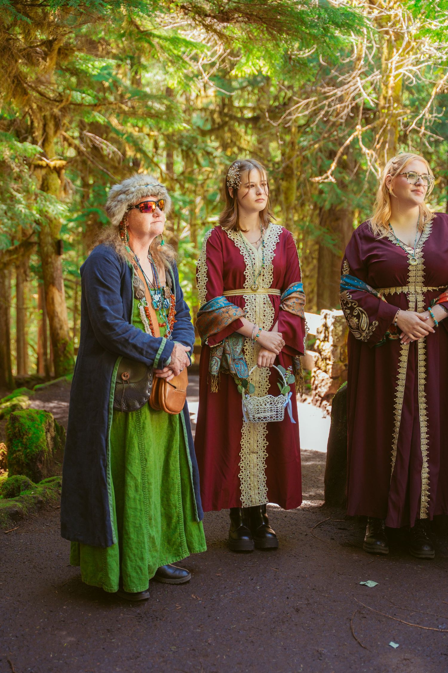 Wedding party members in medieval-inspired dresses of burgundy and green gather in a forest setting.