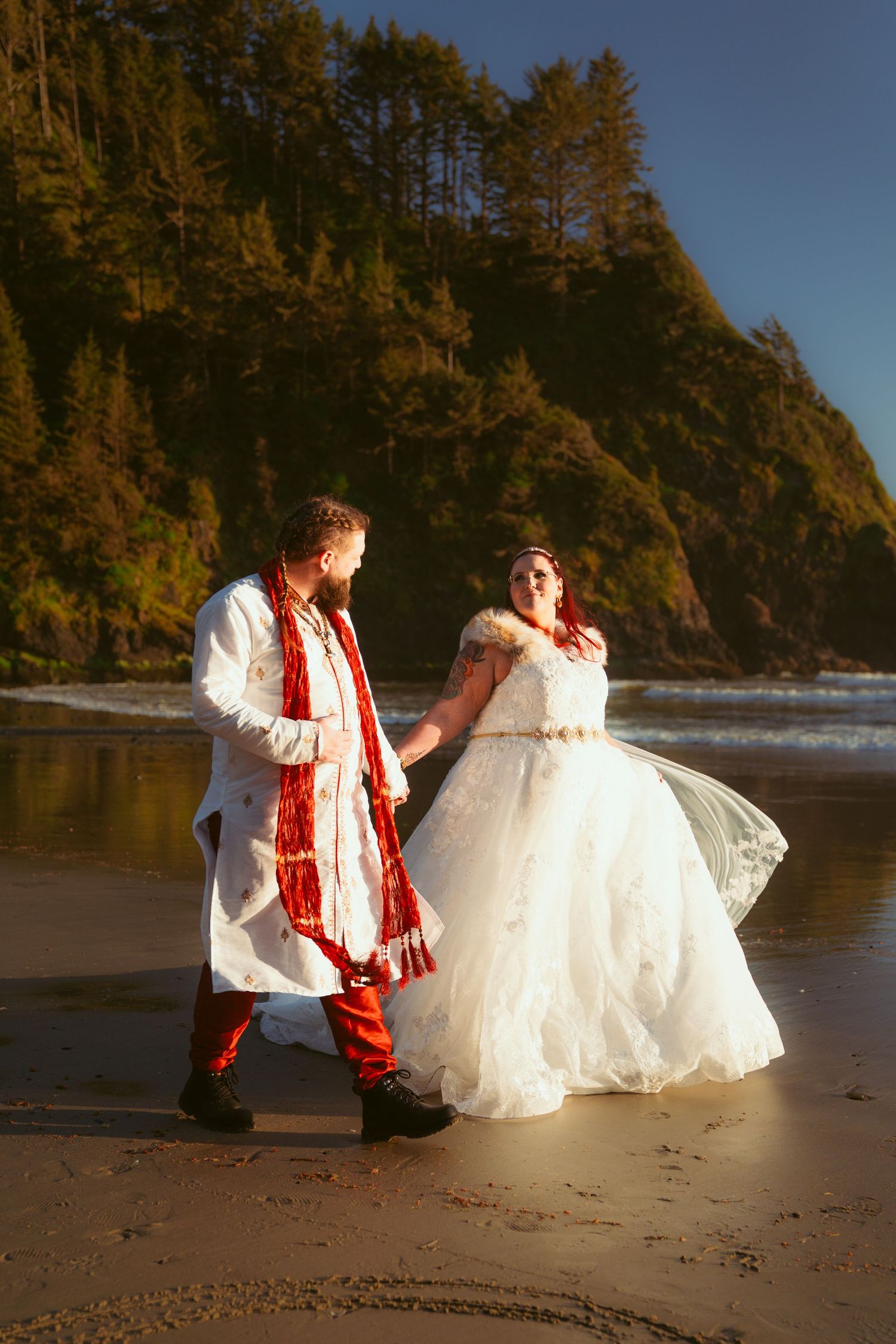 A couple dances on a scenic beach with towering cliffs in the background.