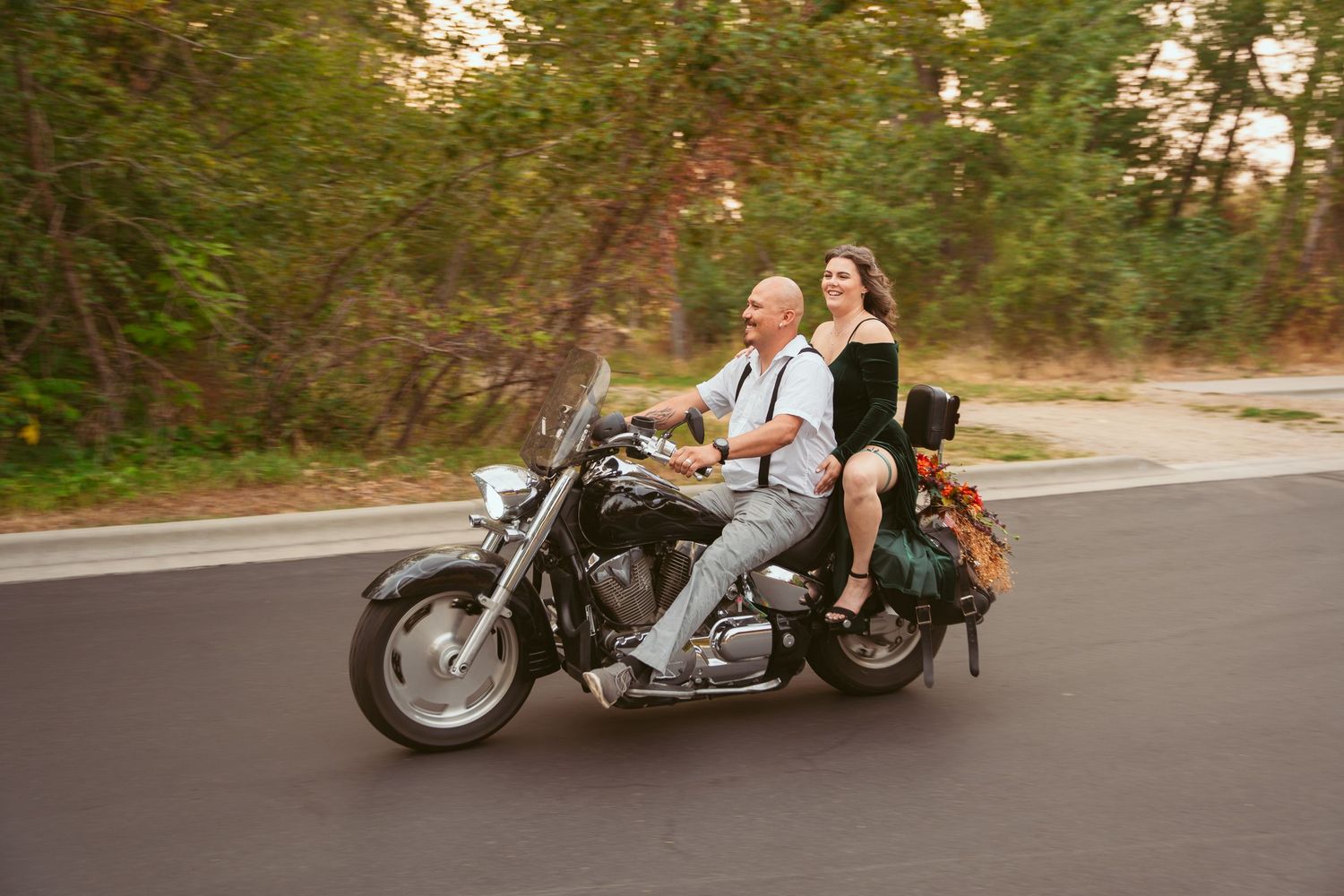 A motorcycle cruises down a tree-lined road during golden hour.