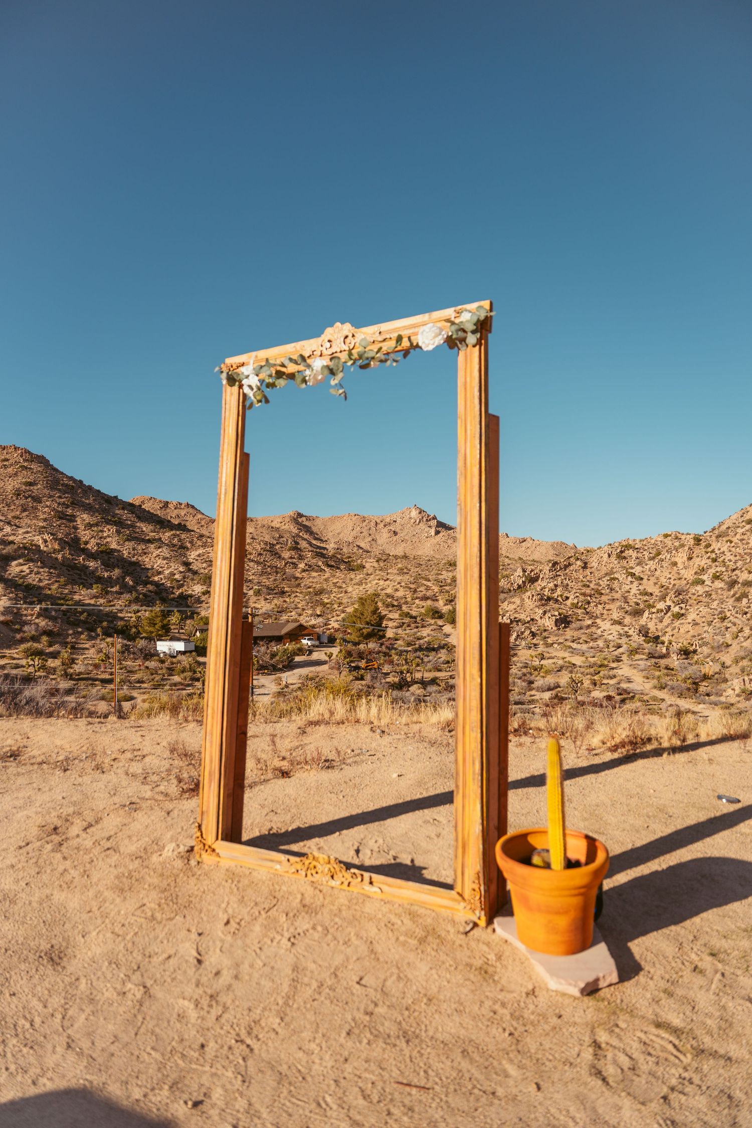 Wooden posts stand in desert sand with mountains in background under blue sky.