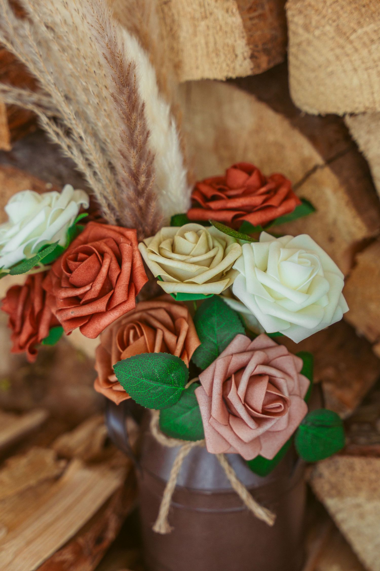 Artificial roses in coral, white and pink arranged in rustic vase with pampas grass.