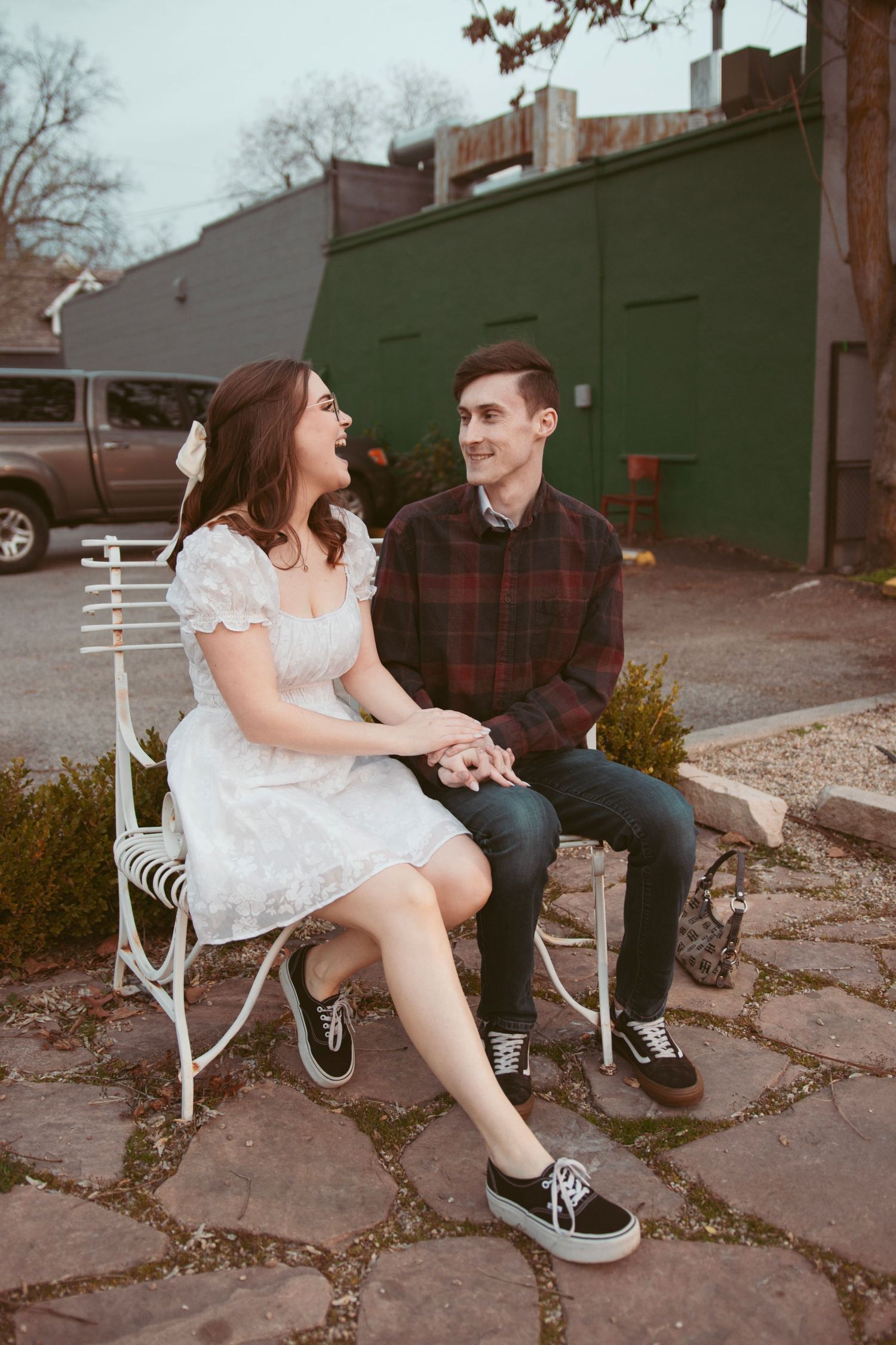 Couple sharing a sweet moment while sitting on vintage white chairs outdoors.