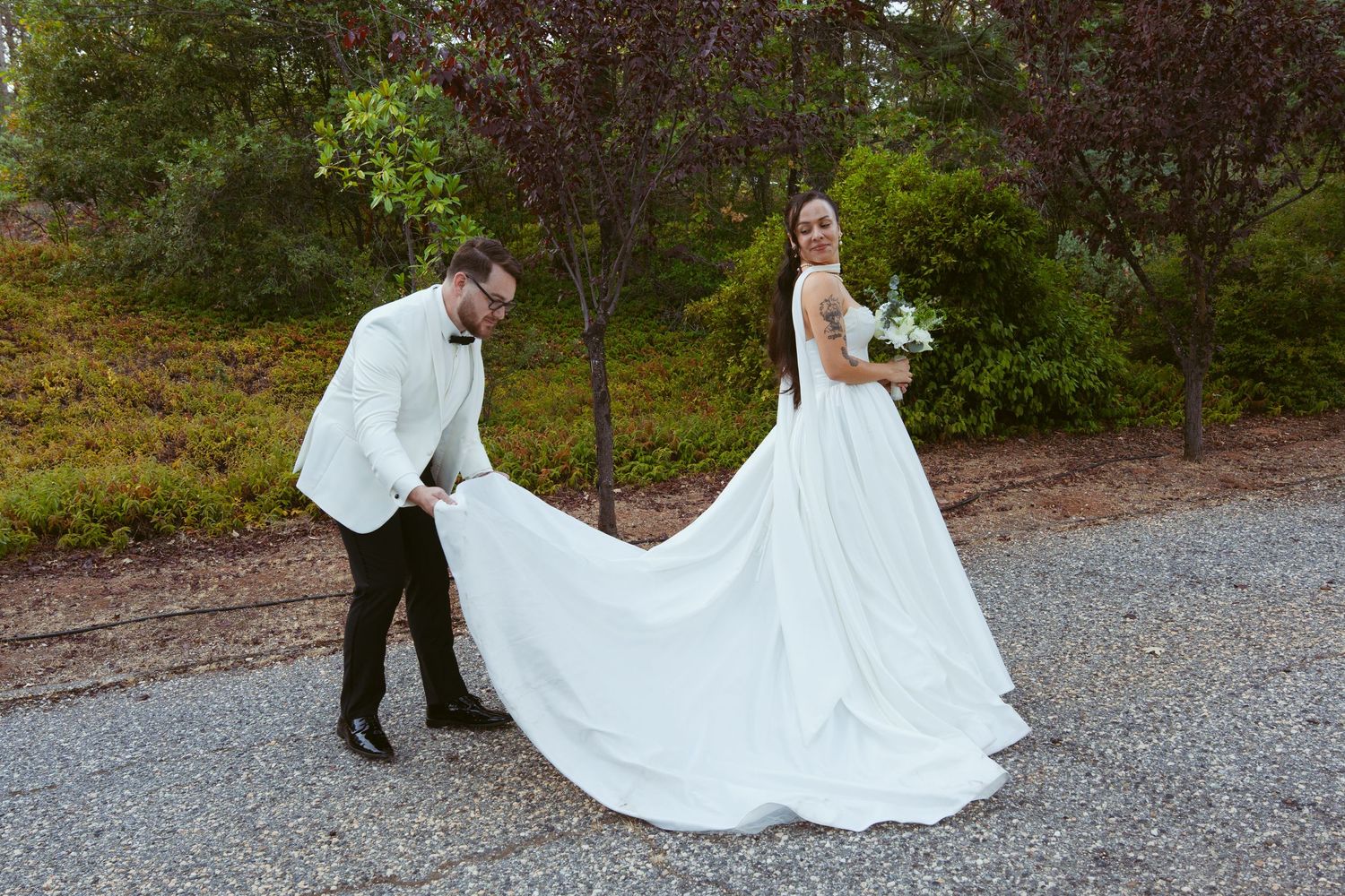 A couple playfully poses with the bride's flowing wedding dress train on a garden path.
