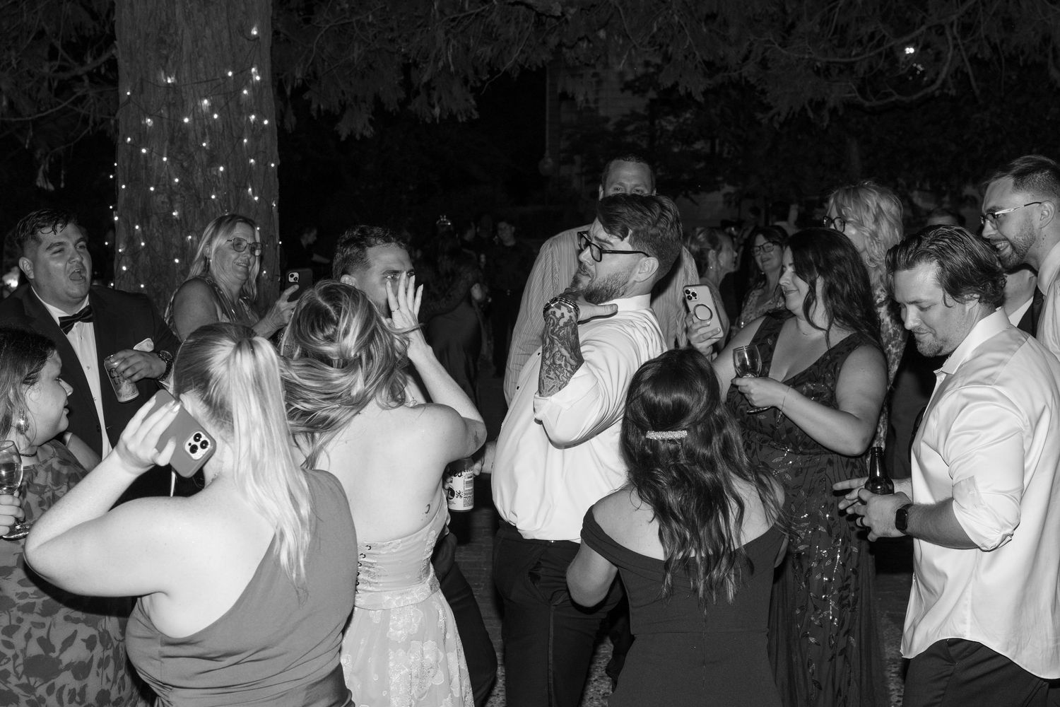 Wedding guests dancing and celebrating at a nighttime reception with string lights overhead.