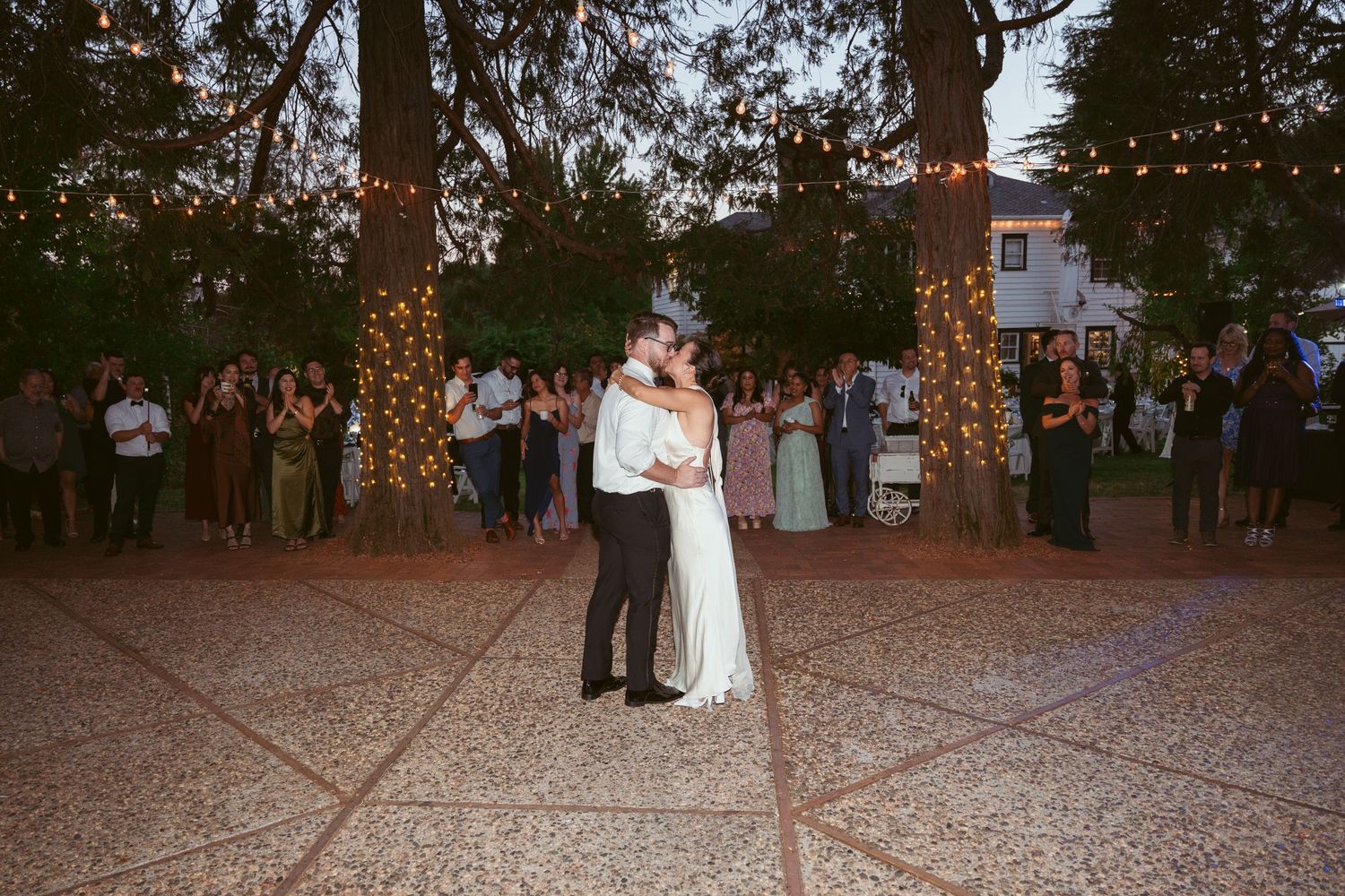Wedding reception dance floor under string lights at dusk.