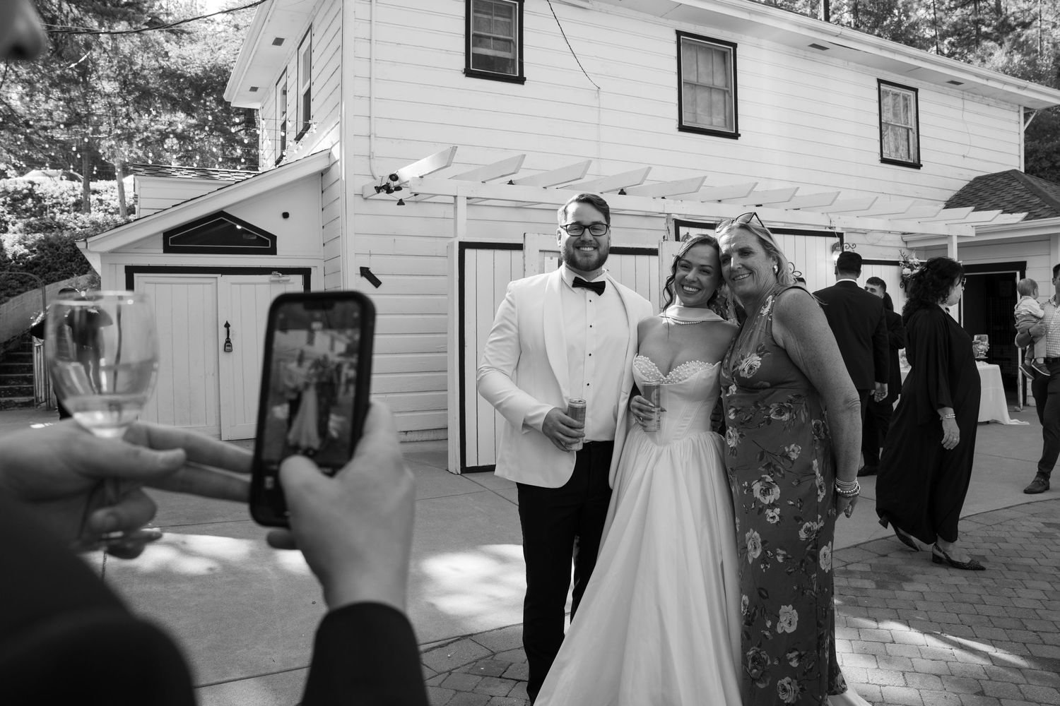 Wedding party members celebrate outside a white building during an afternoon reception.