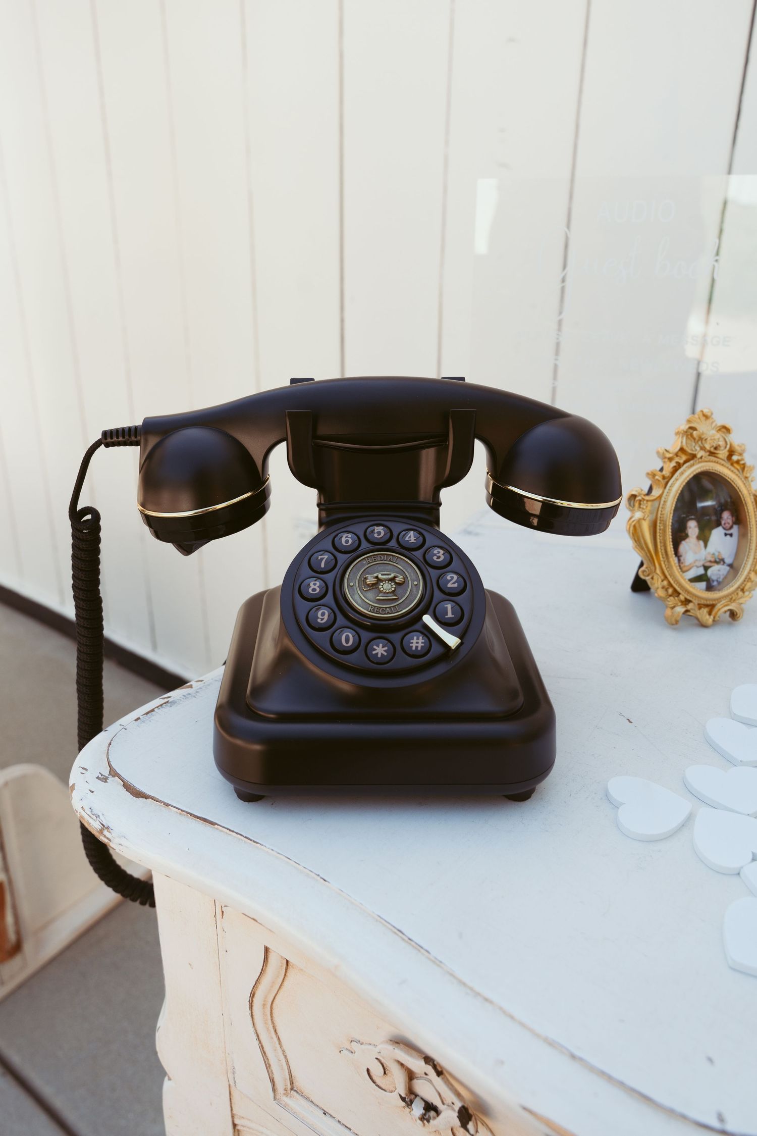 Classic black rotary telephone displayed on white vintage furniture with decorative mirror.