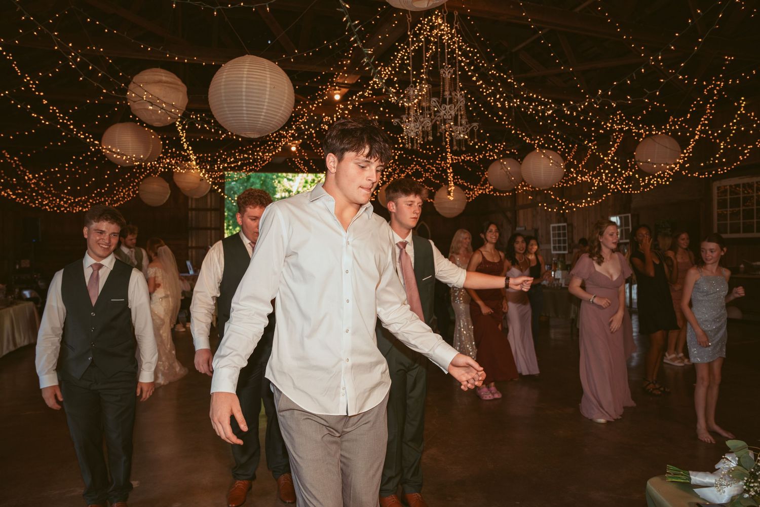 Wedding guests dancing and celebrating under warm twinkle lights and paper lanterns.