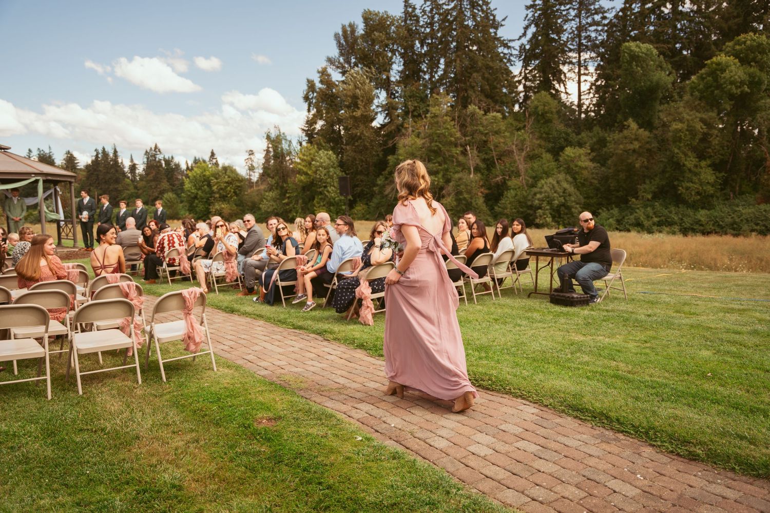 An outdoor ceremony scene with guests seated along a curved brick pathway.