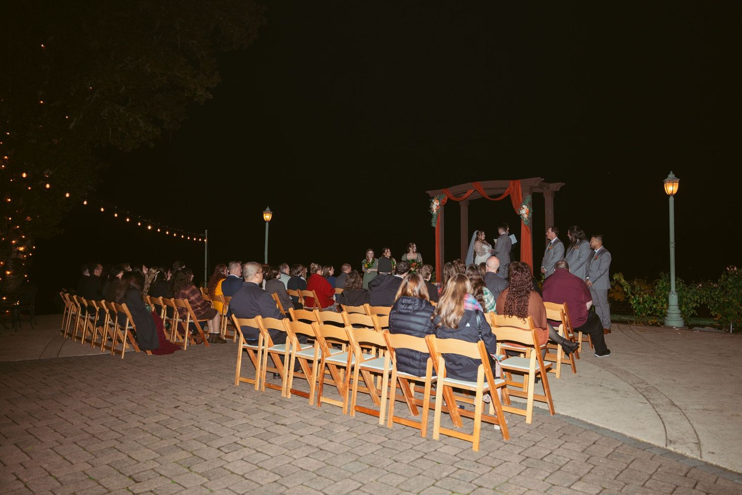 Wedding ceremony setup at dusk with wooden chairs and string lights creating a romantic outdoor atmosphere.