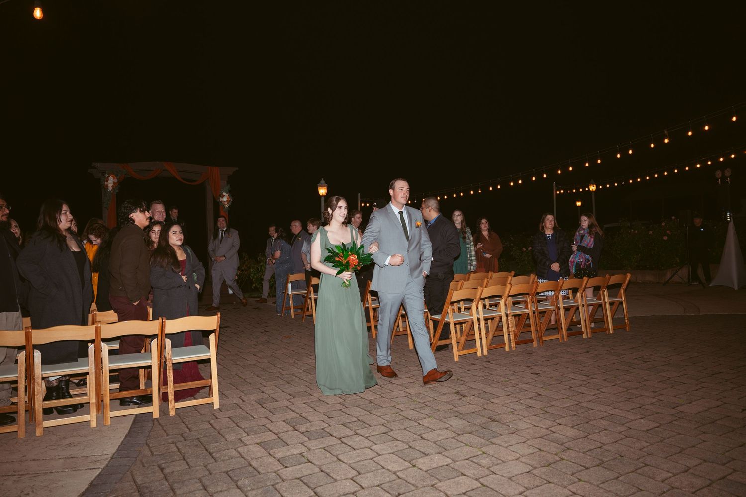 Evening wedding venue with illuminated string lights and rows of wooden chairs.