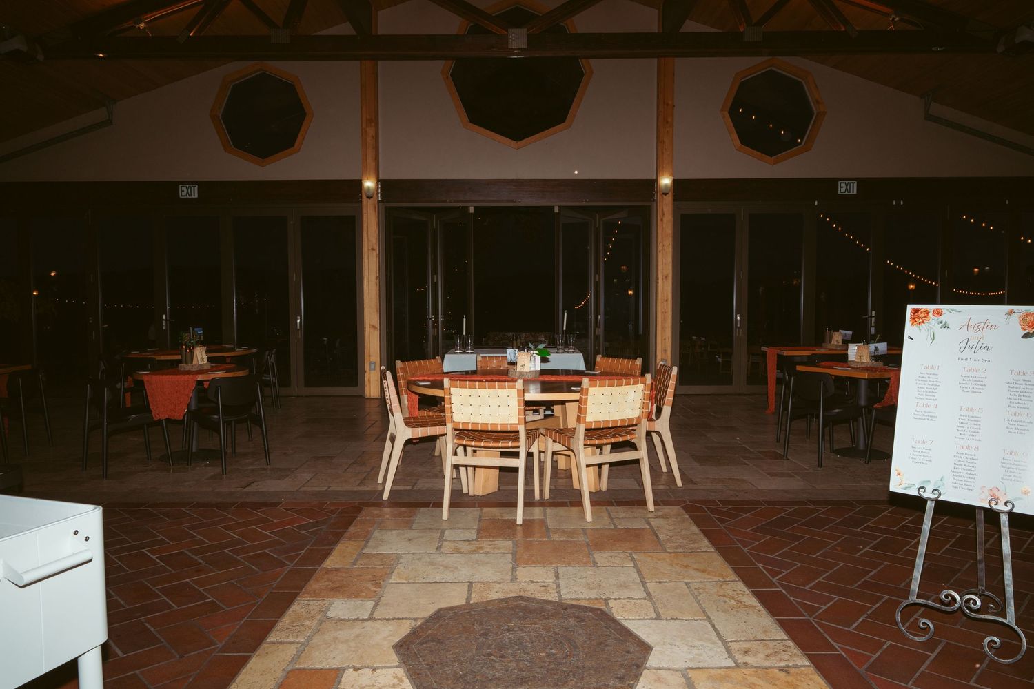 Empty reception hall with wooden chairs and stone flooring in dim lighting.
