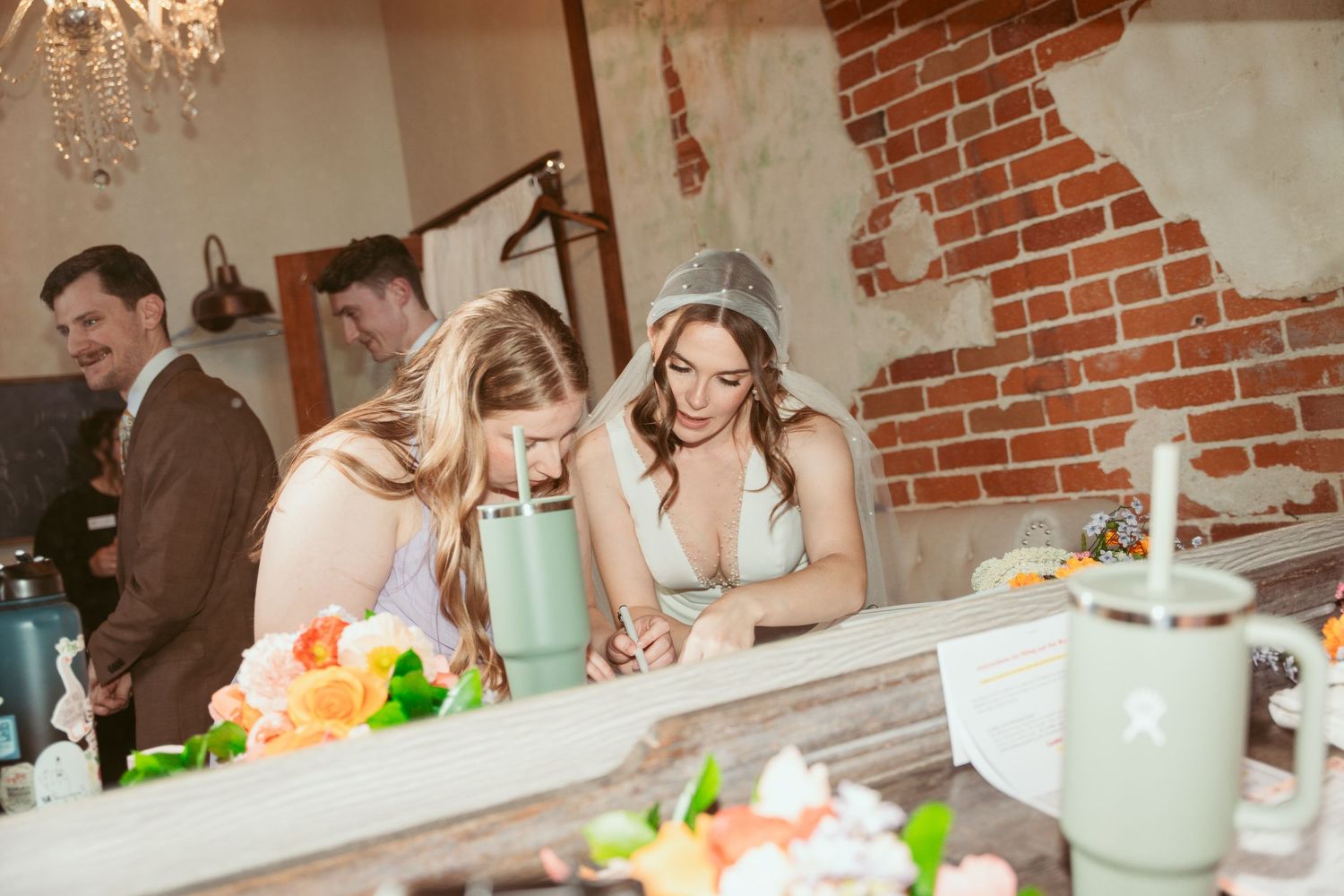 Wedding guests enjoying refreshments at a rustic brick venue with mint green drinks and floral decorations.