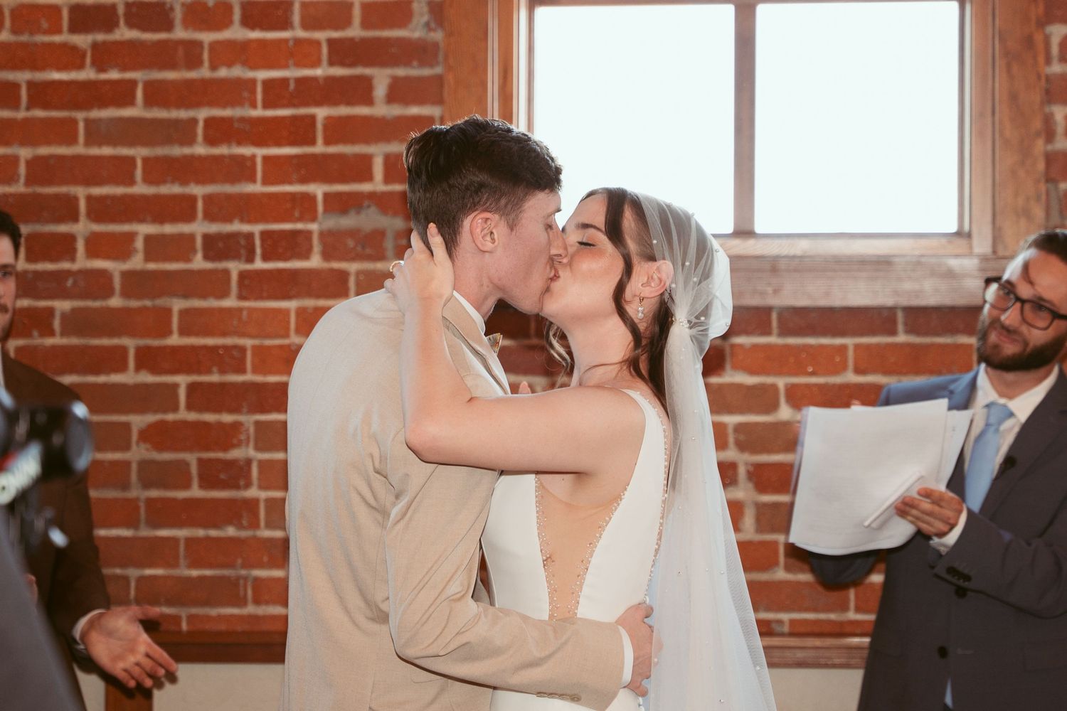 First kiss as newlyweds in front of exposed brick walls and large windows.