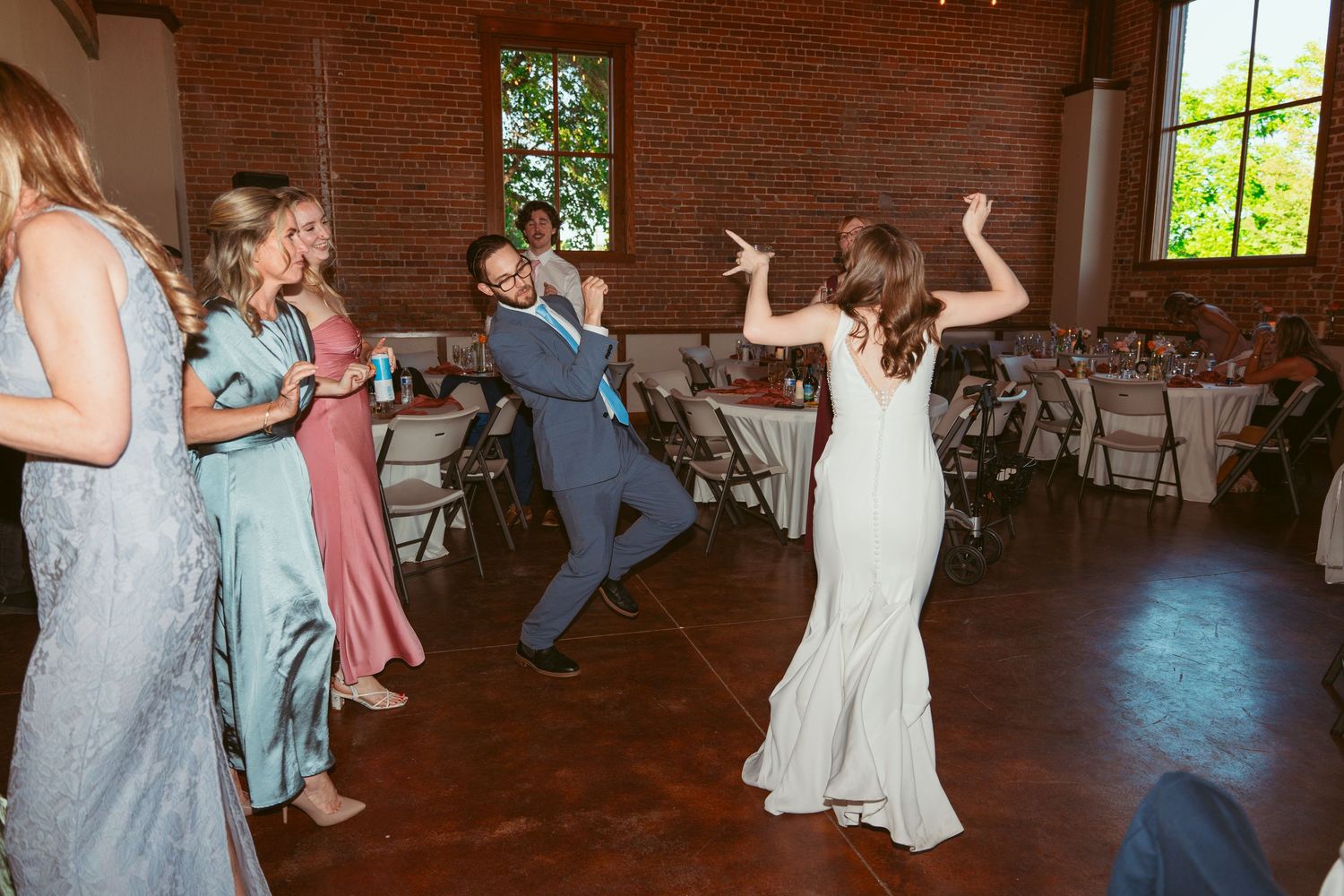 Wedding party dances energetically on the dance floor in a rustic brick venue.