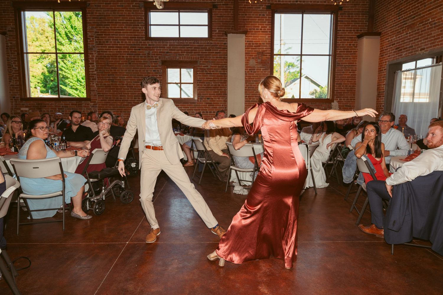 Dancers perform a choreographed routine in a spacious brick-walled reception venue.