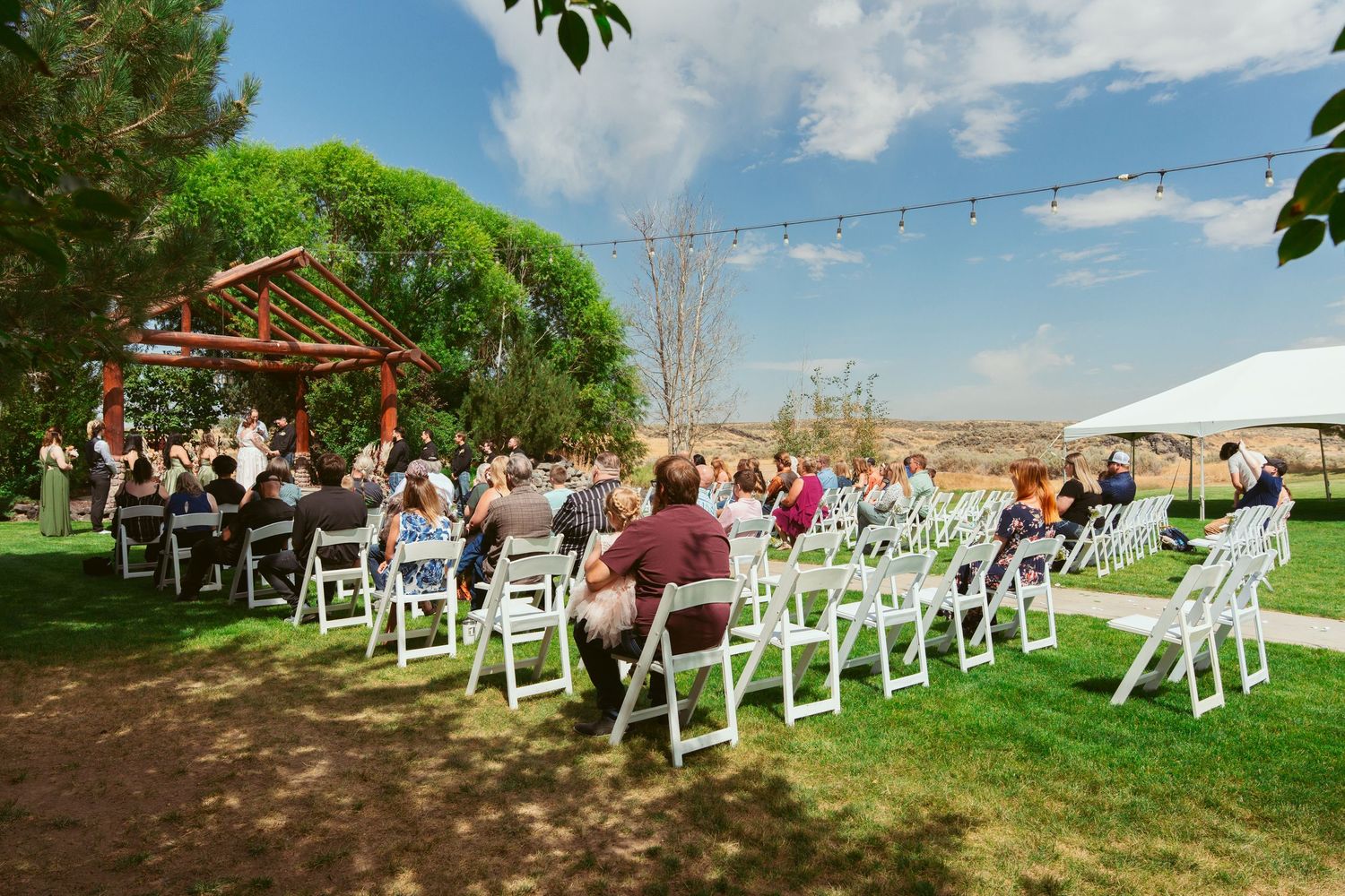 White folding chairs arranged in rows for an outdoor wedding ceremony with green trees and blue sky in the background.