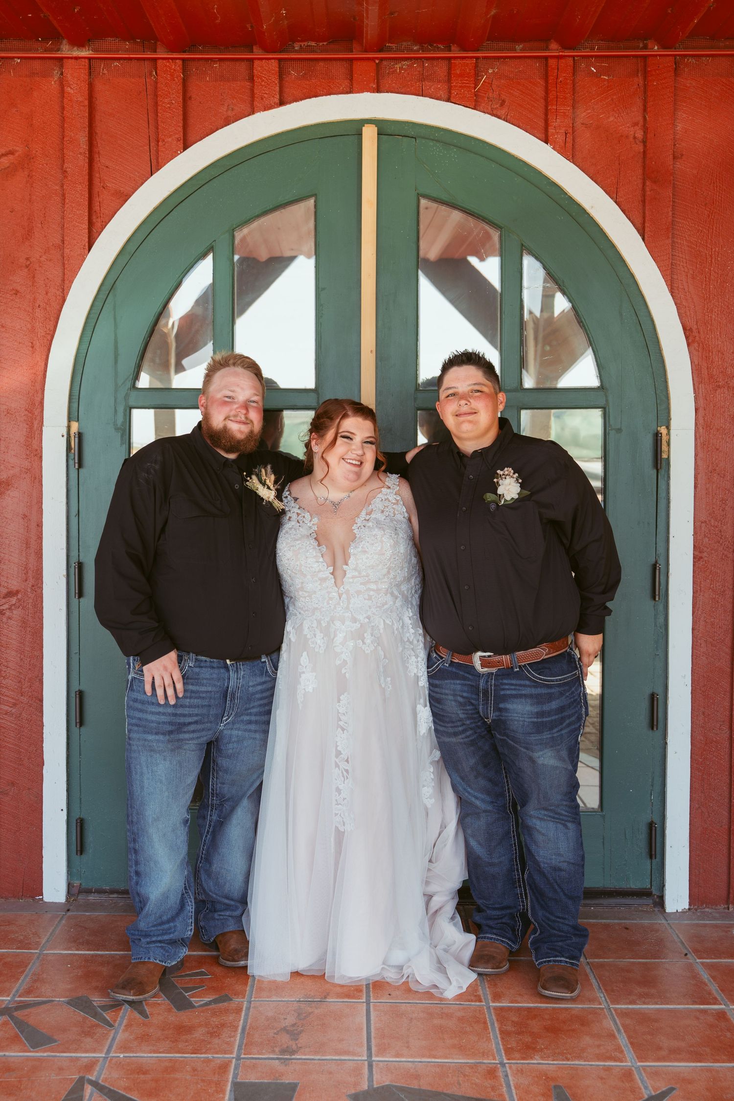 Wedding party poses casually in front of red barn with distinctive teal arched doorways.