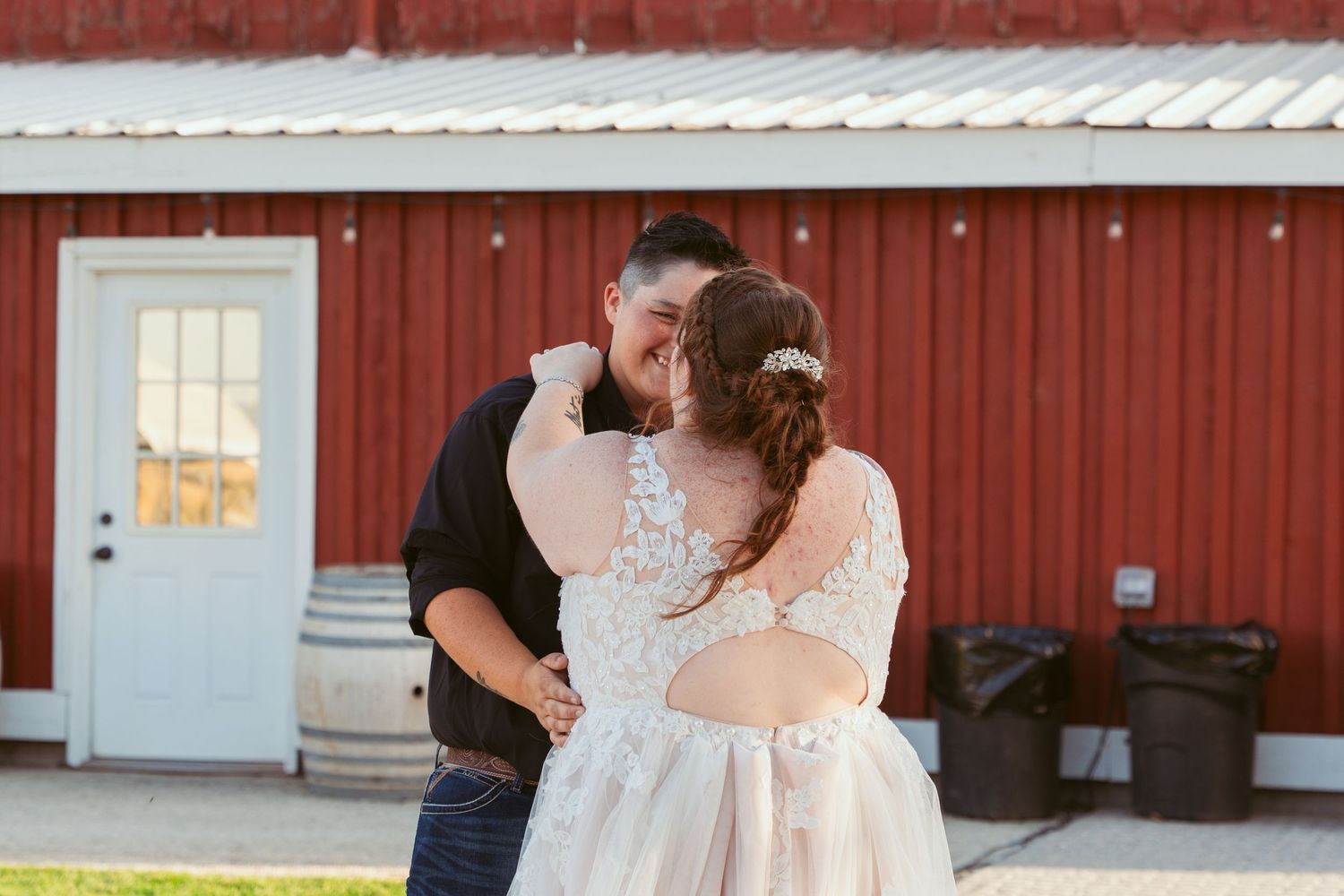 Romantic moment shared between couple in front of a rustic red barn with white trim.