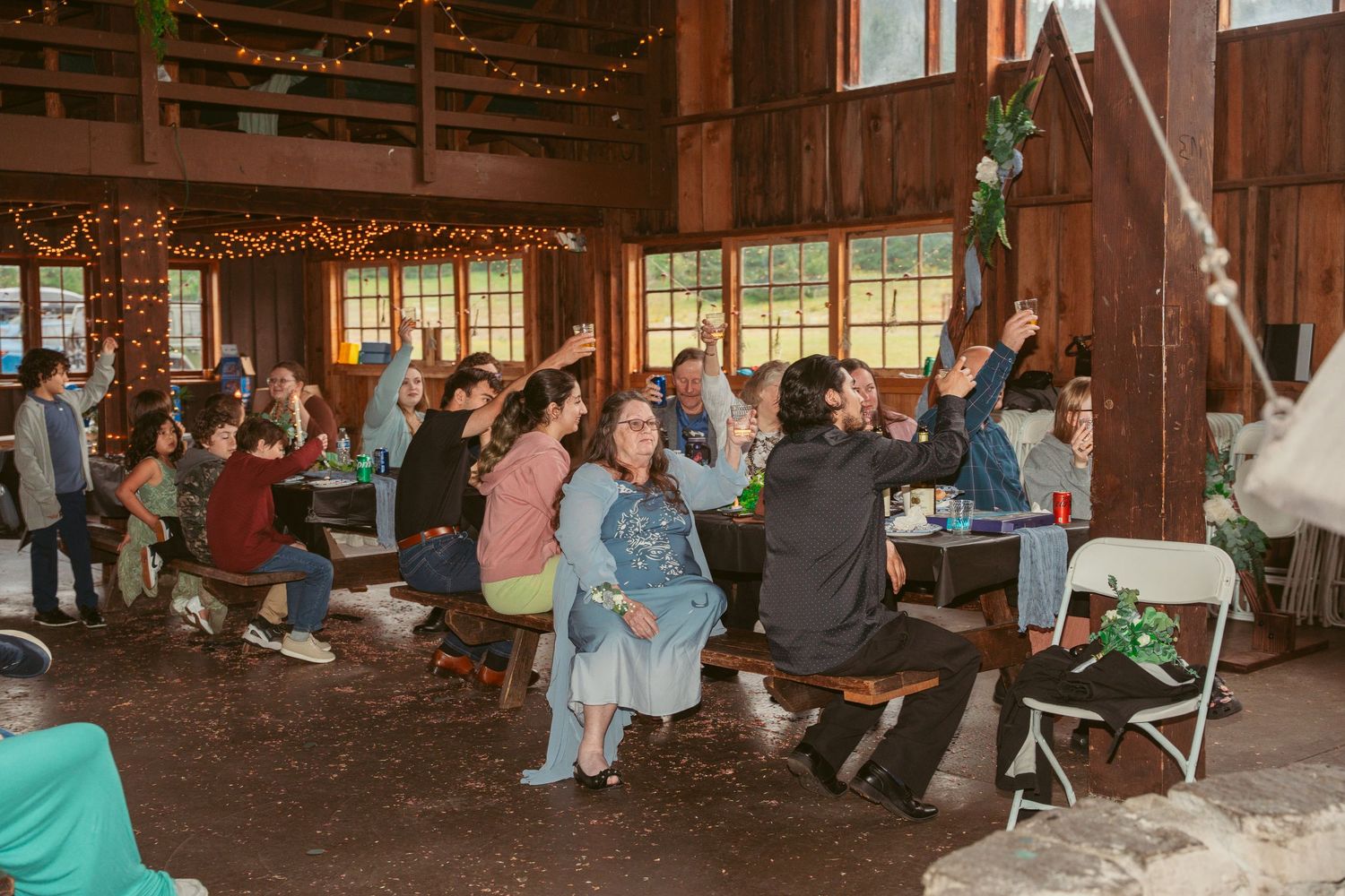 Panoramic view of wedding reception in rustic barn with guests seated at long tables.