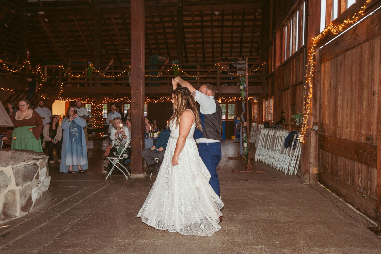 Wedding celebration in a warmly lit wooden barn with guests looking on.