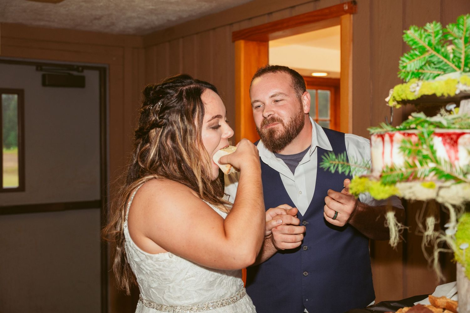 Couple shares a fun cake-cutting moment at their wedding reception in a rustic venue.