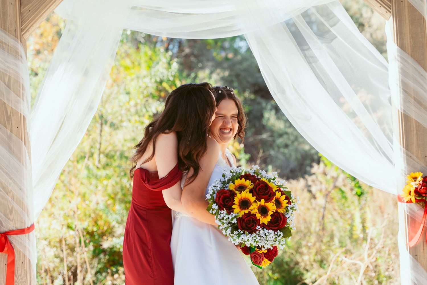Wedding party poses beneath wooden beams decorated with white fabric and sunflowers.