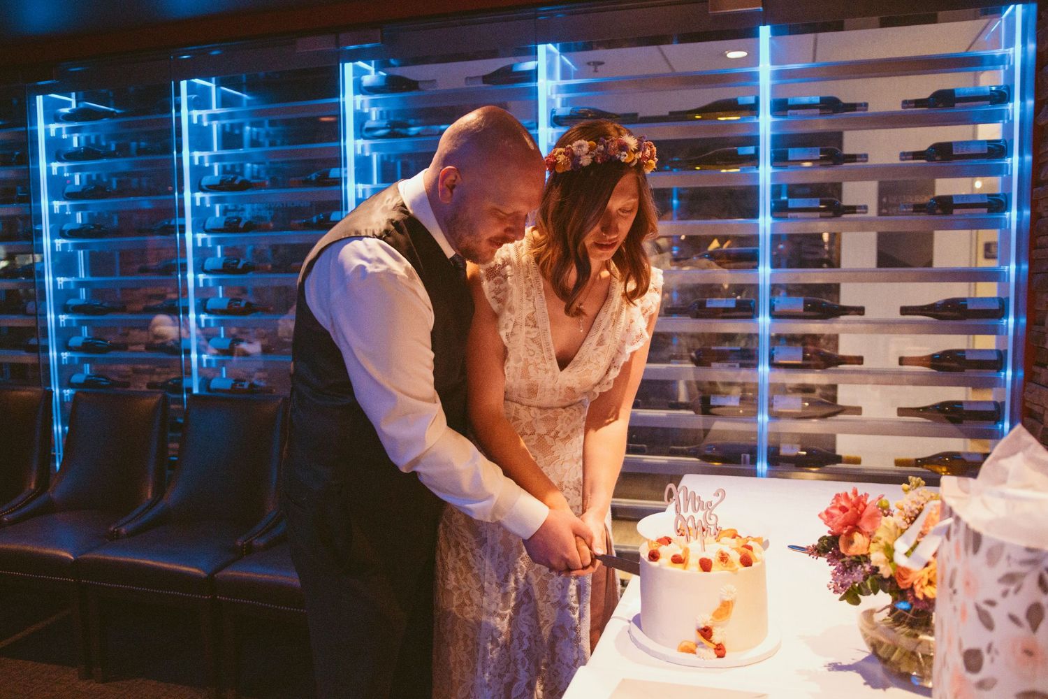 A couple cuts their wedding cake together in front of blue neon lighting.