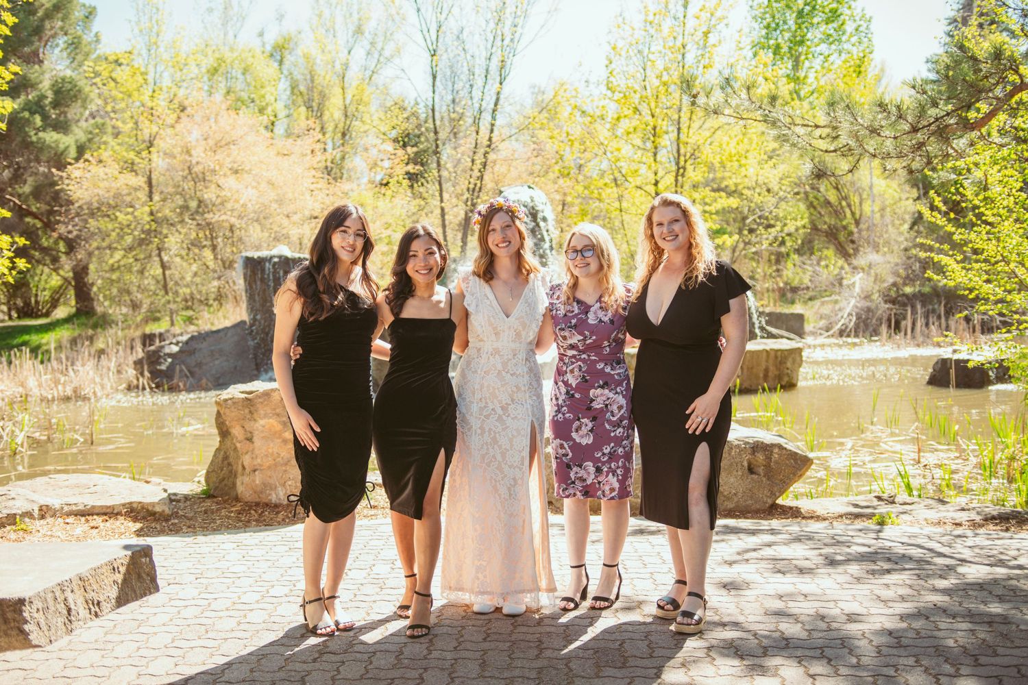 A group poses together at an outdoor wedding venue with stone features and spring foliage.