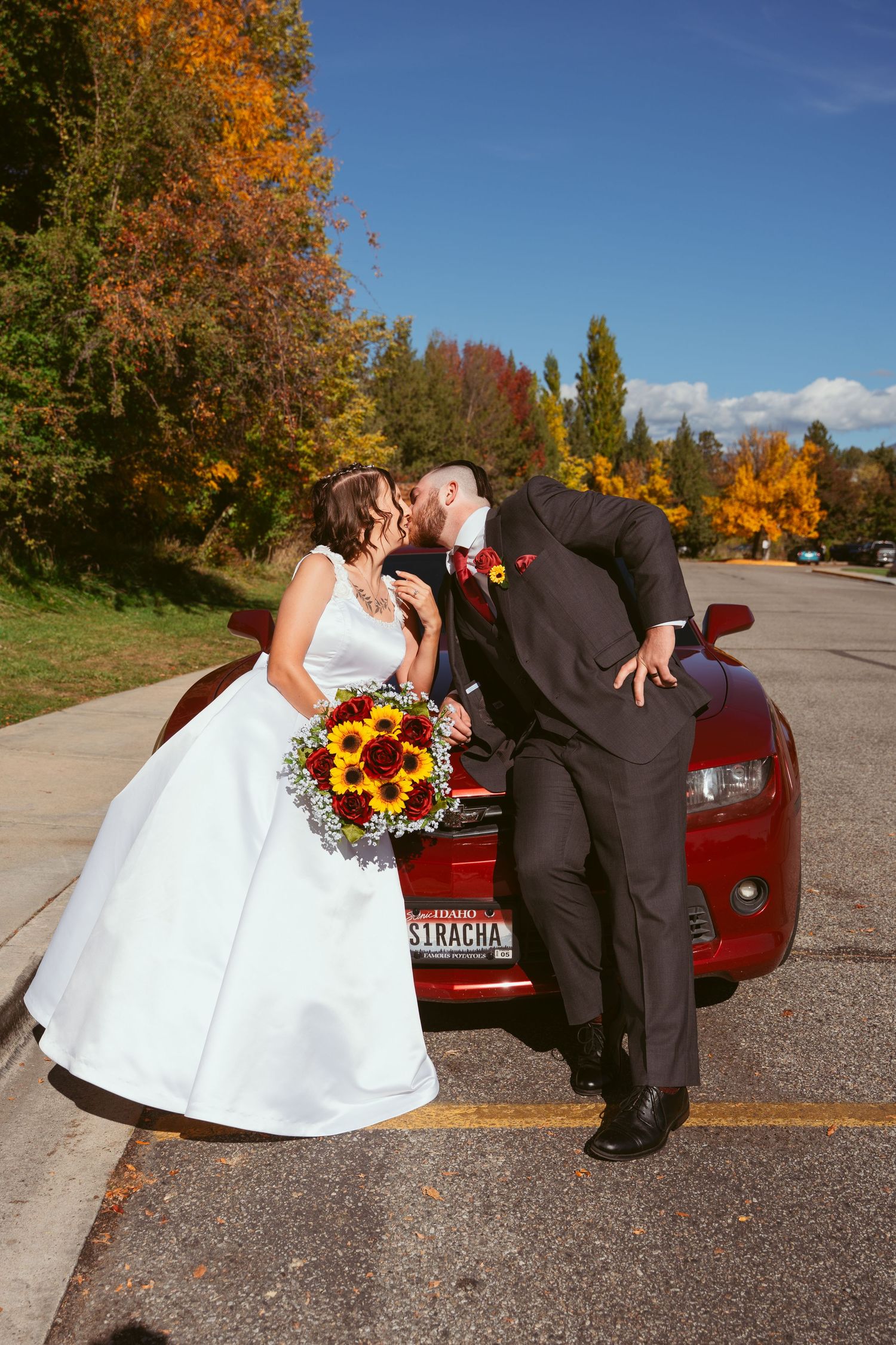 An autumn wedding scene with vibrant fall colors and a red car in the background.