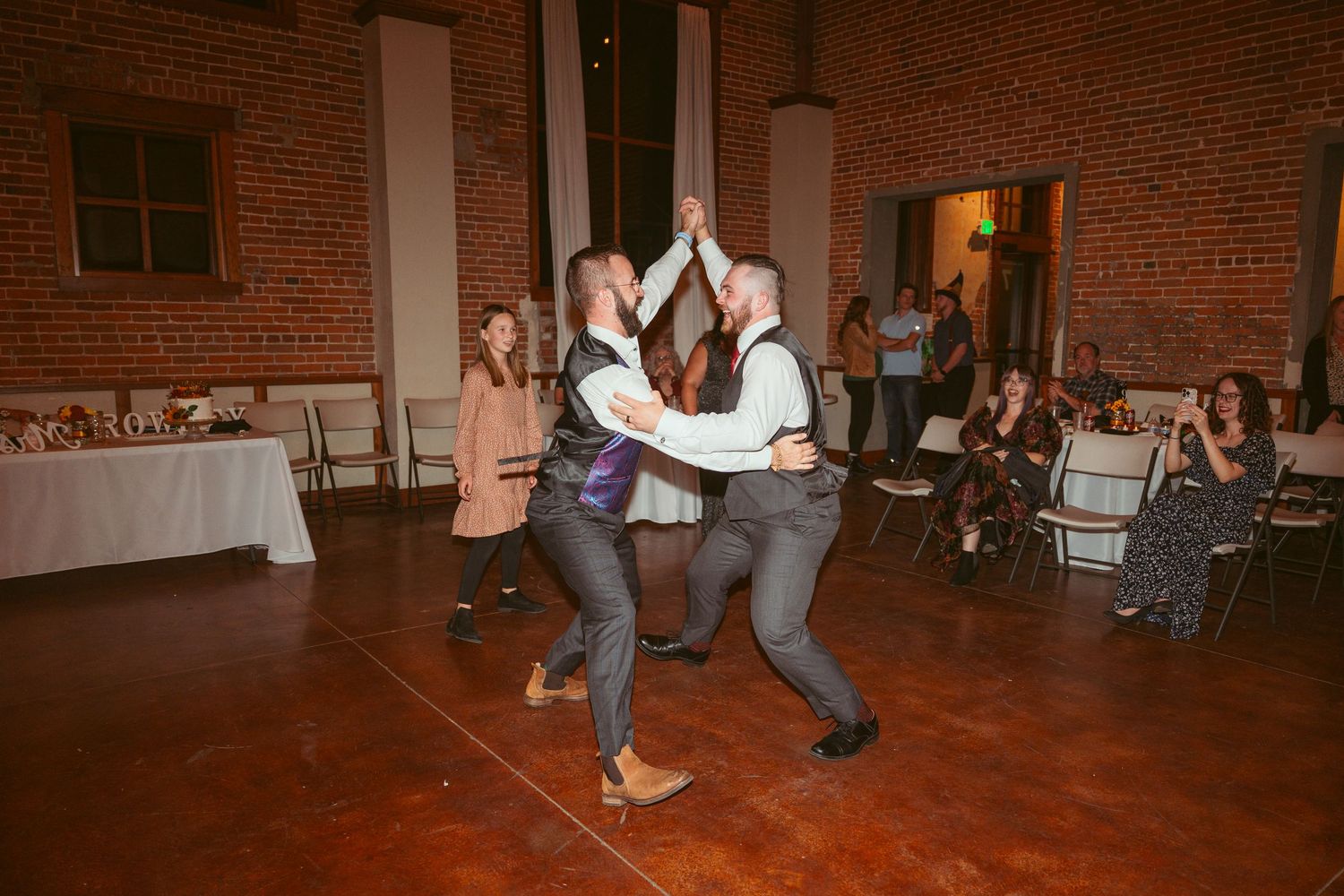 Party guests dancing energetically at a reception in a rustic brick building.