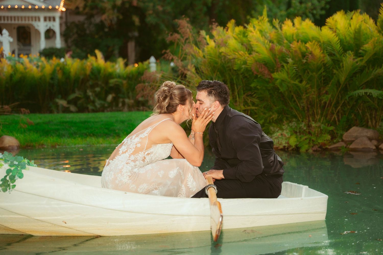 Romantic wedding couple poses together near reflecting pool with lush garden backdrop.