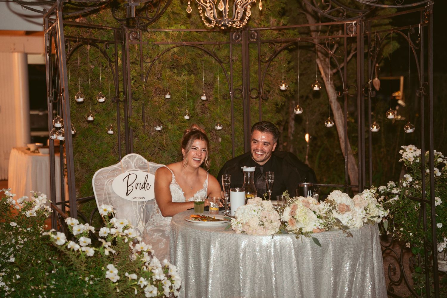 Wedding reception table decorated with elegant white floral arrangements and candles in a rustic indoor venue.
