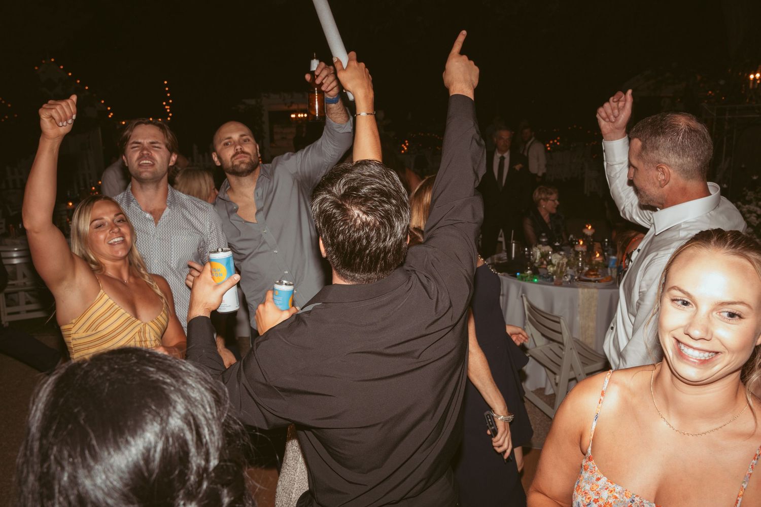 Party guests raise their hands and drinks in celebration at a nighttime event.