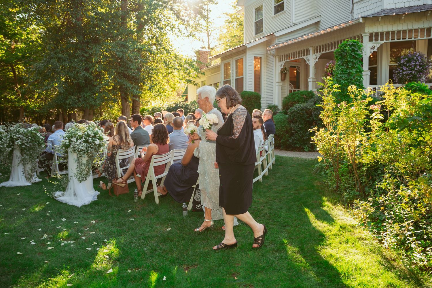 Beautiful outdoor wedding ceremony setup on a lawn with white chairs and natural sunlight filtering through trees.