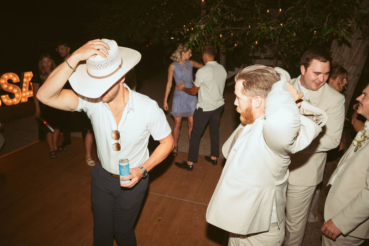 Lively dance party at an outdoor wedding reception with illuminated decor.